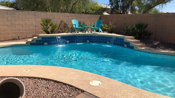 A swimming pool with blue tiles, two turquoise chairs, and a brick wall. - Oasis Pool and Backyard!  Johnson Ranch Golf Course  (San Tan Valley)