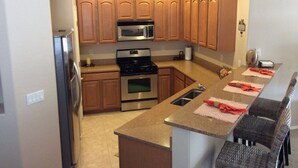 A modern kitchen with wooden cabinets, stainless steel appliances, and a breakfast bar with wicker chairs. - Oasis Pool and Backyard!  Johnson Ranch Golf Course  (San Tan Valley)