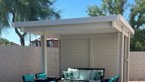 An outdoor patio with a covered seating area, a stone pathway, and a well-maintained lawn. - Oasis Pool and Backyard!  Johnson Ranch Golf Course  (San Tan Valley)