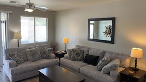 A living room with a grey sofa set, a coffee table, two side tables with lamps, a ceiling fan, and a framed artwork on the wall. - Oasis Pool and Backyard!  Johnson Ranch Golf Course  (San Tan Valley)