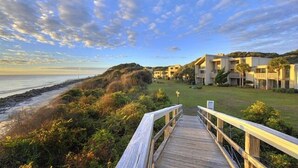 Um hotel à beira-mar com uma passarela de madeira que dá para a praia, com arquitetura moderna e um gramado.