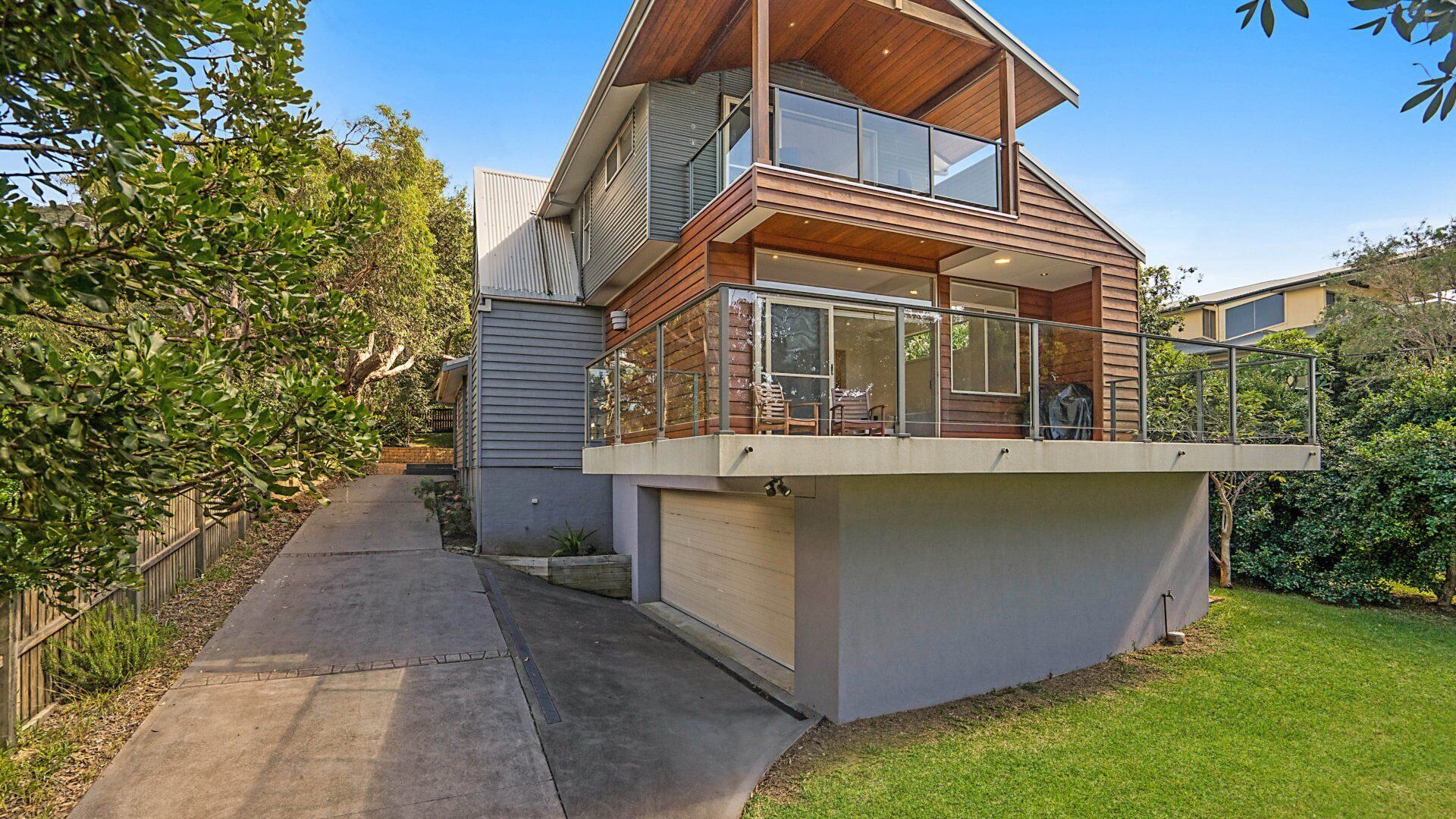 A modern two-story house with a glass balcony and a covered outdoor seating area.