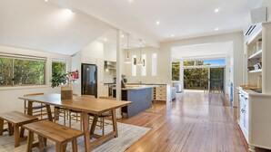 A spacious kitchen with a central island, wooden flooring, and large windows offering views of greenery. - Eucalyptus Beach House by HolidayCo. (KILLCARE)
