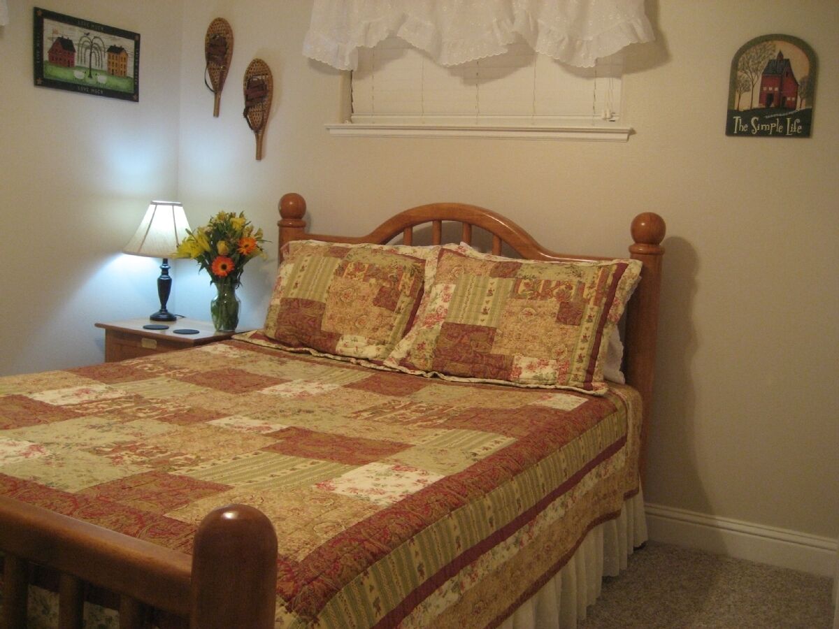 A bedroom with a wooden bed, floral bedding, a nightstand with a lamp, and wall decorations.