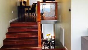 Uma escadaria leva a uma varanda com vista, uma área de refeições com mesa e cadeiras e uma sala de estar com sofá.