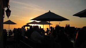 Vista do pôr do sol a partir de um terraço com guarda-sóis e pessoas sentadas.