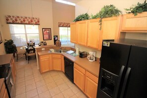 A kitchen with wooden cabinets, a black refrigerator, a coffee maker, and a dishwasher. - Huge 6 Bedroom Home in Gated Cypress Pointe Forest - CP001 (Davenport)