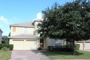 A two-story residential house with a garage, a driveway, and a large tree in the front yard. - Huge 6 Bedroom Home in Gated Cypress Pointe Forest - CP001 (Davenport)