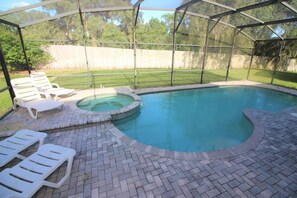 A covered swimming pool with a hot tub, surrounded by a brick patio and white lounge chairs. - Huge 6 Bedroom Home in Gated Cypress Pointe Forest - CP001 (Davenport)
