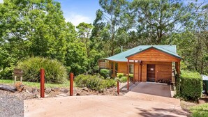 A wooden cabin with a green roof, surrounded by lush greenery and trees.