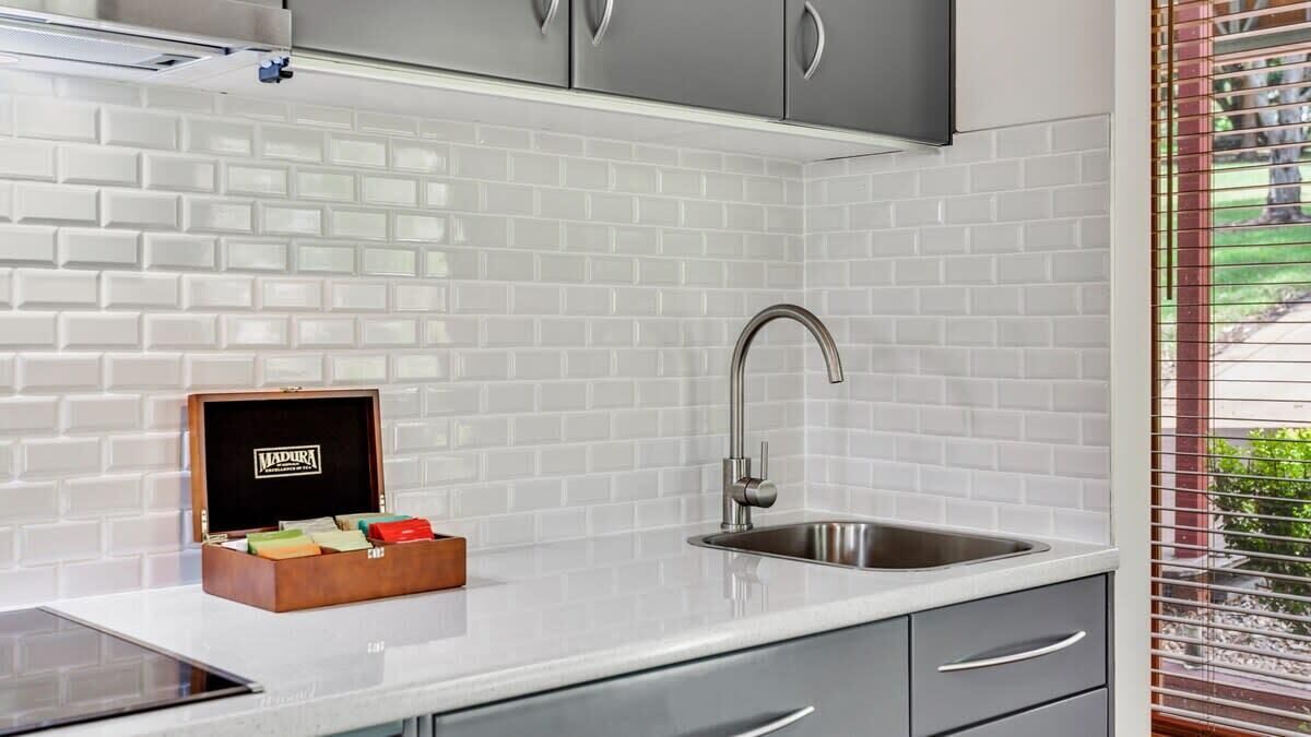 Una cocina moderna con azulejos blancos tipo metro, un lavamanos de acero inoxidable y una caja de madera con objetos.