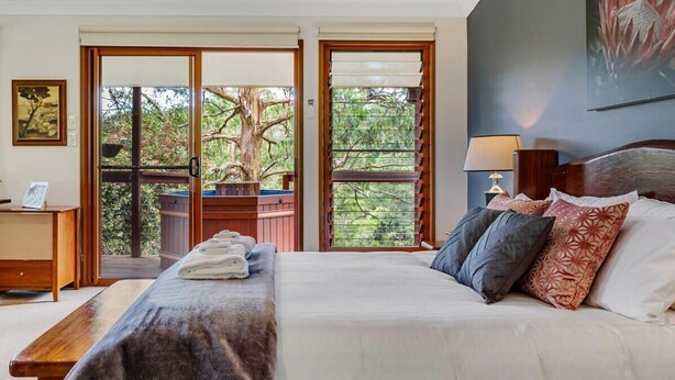 A bedroom with a bed, pillows, a nightstand, a lamp, and a view of the outdoors through a sliding door.
