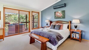 A bedroom with a large bed, a bench, a hot tub outside the sliding glass door, and a bookshelf.