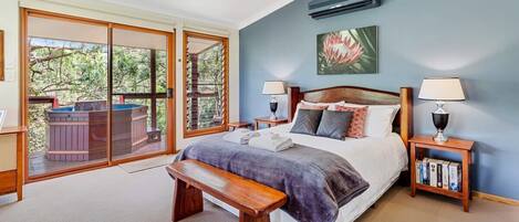 Een slaapkamer met een groot bed, een bankje, een bubbelbad buiten de schuifdeur en een boekenkast.