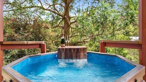 A hot tub with a bottle and glasses on a wooden platform surrounded by trees.