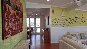A spacious living room with a wooden floor, a white sofa, and a dining area with a table and chairs.