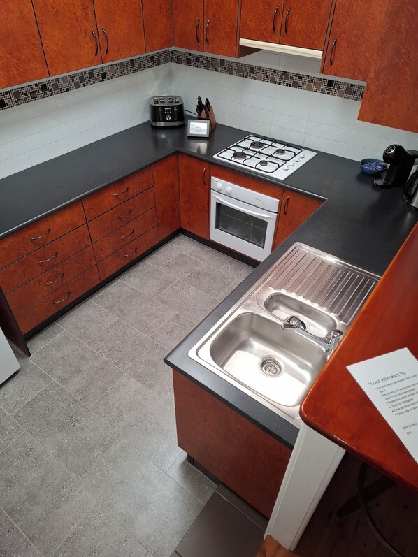 A kitchen with wooden cabinets, a gas stove, an oven, and a stainless steel sink.