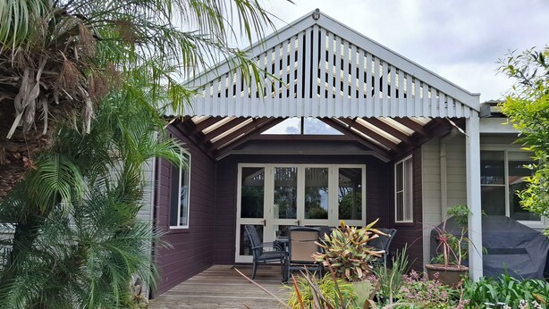 A covered patio with a wooden deck, a table and chairs, and various plants.