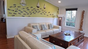 A living room with a beige sofa, a wooden coffee table, and a wall decorated with fish and sailboat wall art.