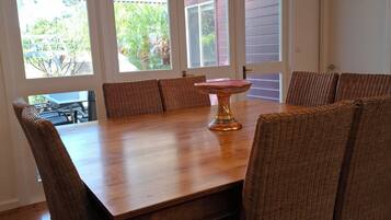 A dining area with a wooden table and wicker chairs, large windows with a view of greenery, and a ceiling fan.