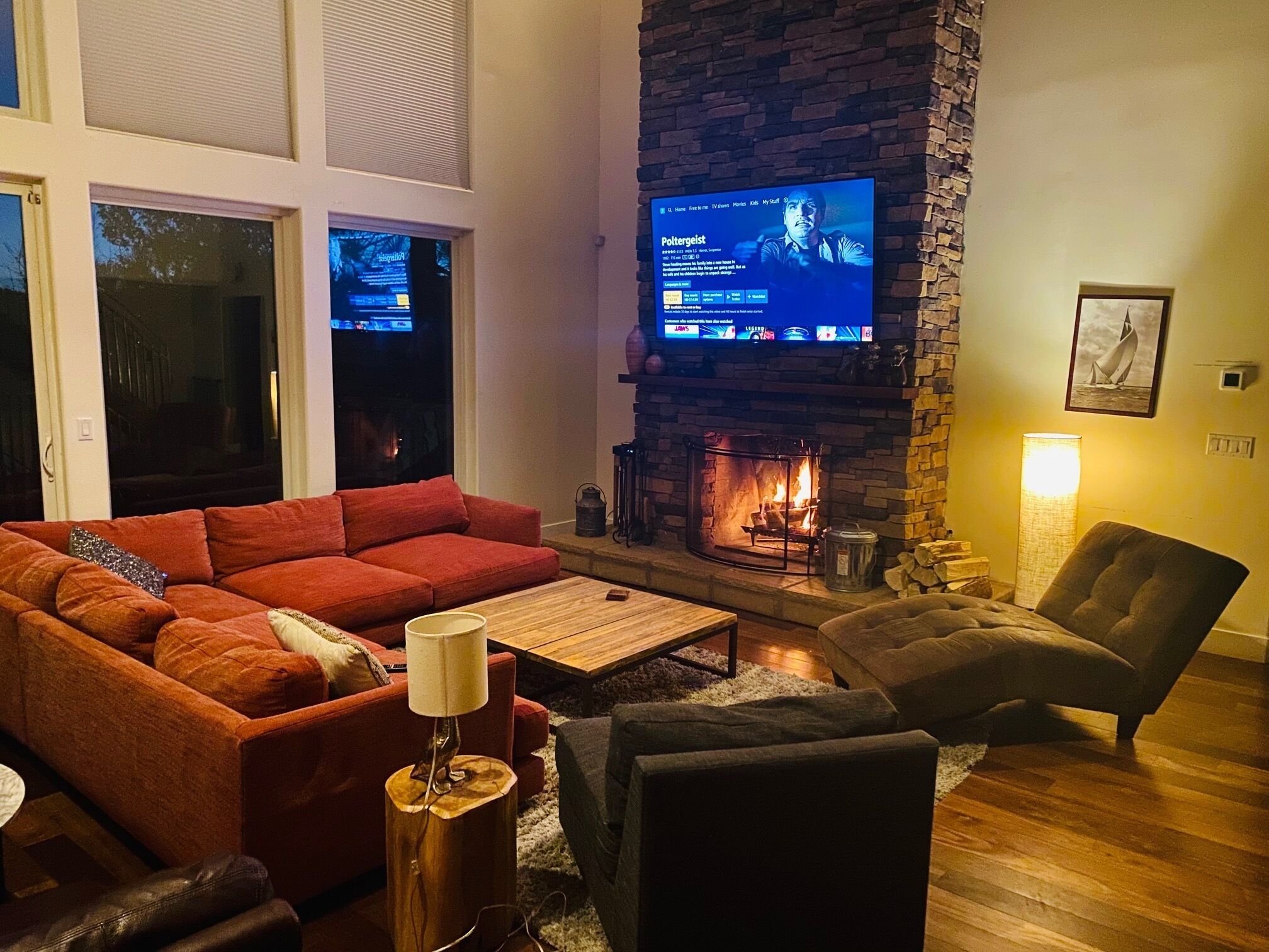 A living room with a stone fireplace, a red sofa, a wooden coffee table, and a television mounted on the wall.