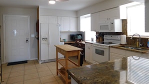 A modern kitchen with white cabinets, a wooden table, a microwave, a stove, and a ceiling fan. - Spectacular Beach Cottage, Pet Friendly, Gulf Views, Great for Families (Fort Myers Beach)