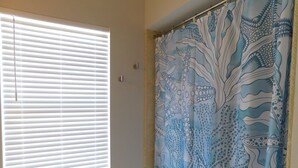 A bathroom with a window with blinds, a shower curtain with a marine life pattern, and a plain wall. - Spectacular Beach Cottage, Pet Friendly, Gulf Views, Great for Families (Fort Myers Beach)