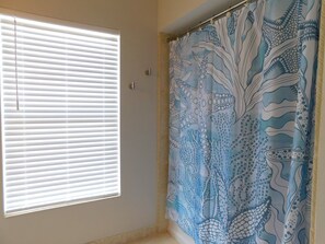 Une salle de bain avec une fenêtre équipée de stores, un rideau de douche orné de motifs représentant la vie marine et un mur uni.
