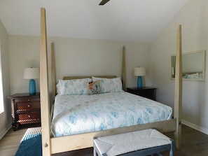 Una cama con dosel, un edredón estampado, dos mesitas de noche con lámparas, un banco de madera y un espejo en la pared.