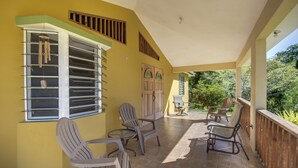 Une terrasse couverte avec des sièges d’extérieur, une fenêtre avec des stores et une porte dotée d’une fenêtre.