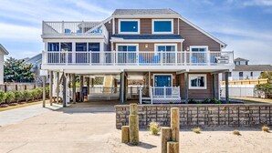 Une maison de plage à deux étages, dotée d’un patio couvert, d’une porte bleue et d’un panneau indiquant les éléments essentiels à la survie dans la nature (en référence aux ours).