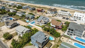 Vue aérienne d’un quartier résidentiel situé sur la côte, avec des maisons, une plage et une grande piscine.