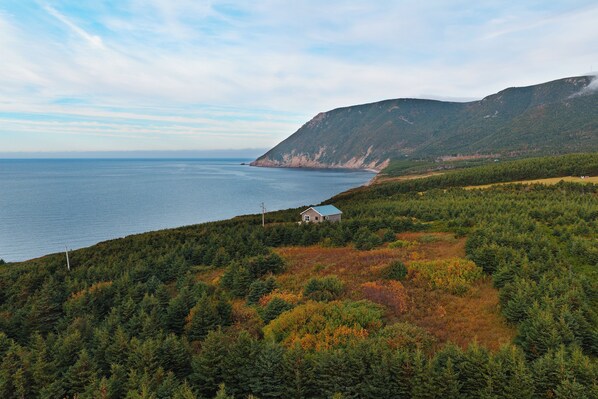 A coastal landscape with a house on a hill overlooking the sea.