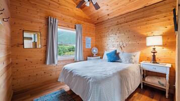Une chambre dans une cabane en bois, avec un lit, une table de chevet, une lampe et une fenêtre avec des rideaux.