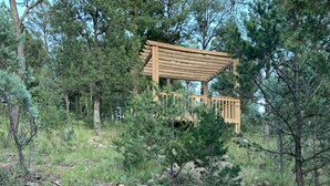 A wooden pergola structure surrounded by a natural landscape with a dirt path and scattered rocks. - Mountain-side Cabin with hot tub! Close To Town And Skiing on 1.1 acres.  (Ruidoso)