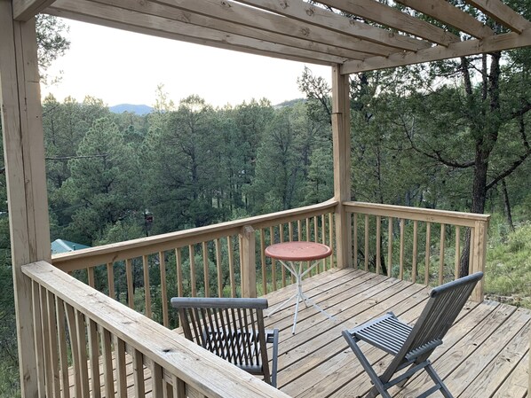 A wooden deck with two chairs and a small table, overlooking a forested area.