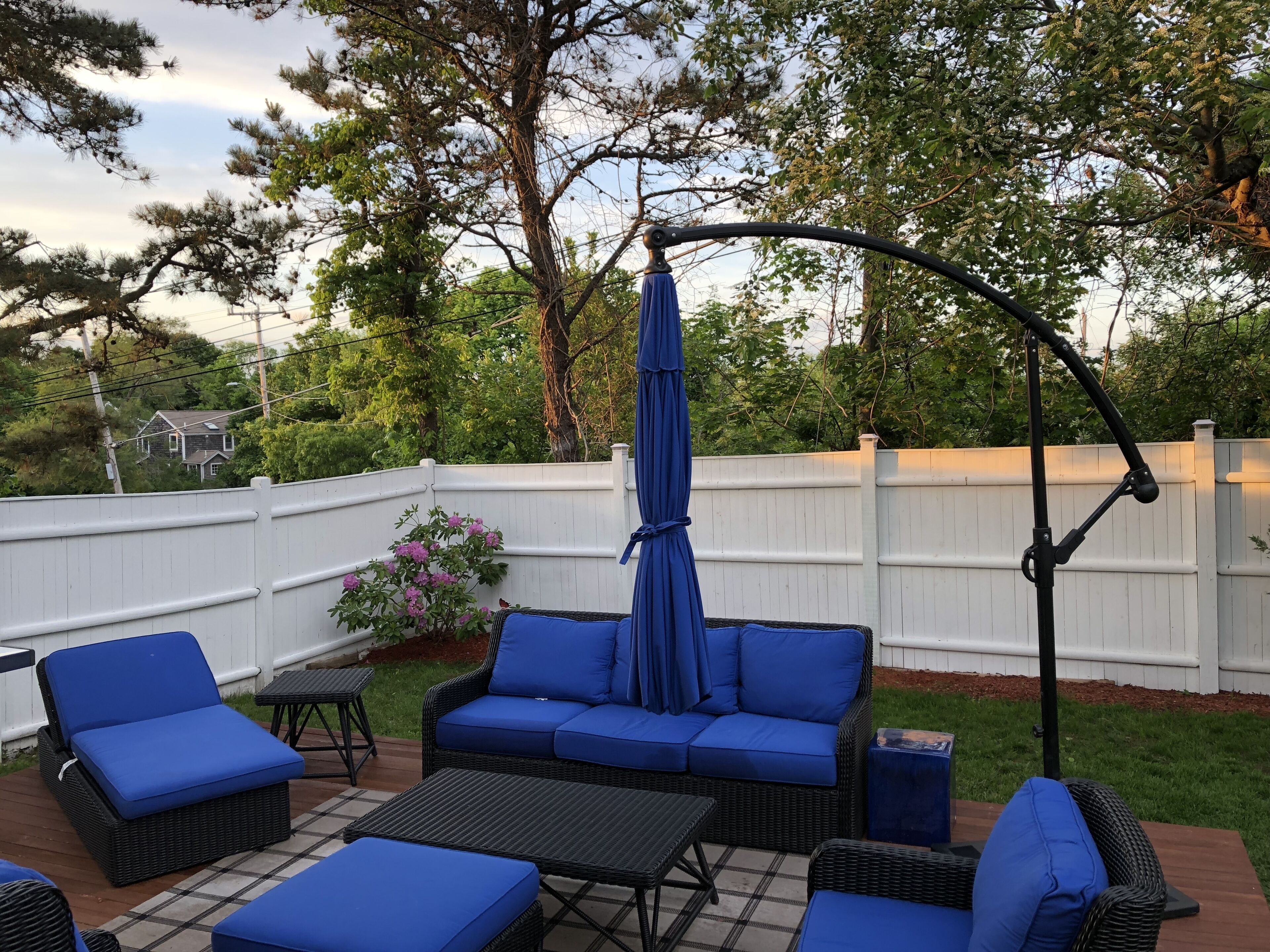 An outdoor patio with wicker furniture, a hanging umbrella, and a white fence.