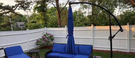 An outdoor patio with wicker furniture, a hanging umbrella, and a white fence.