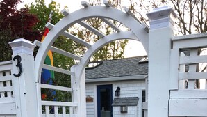 A white wooden gate with a lattice design, leading to a house with a blue door and a small porch. - Beautiful Free-Standing Cottage, In The Heart of Provincetown.  (Provincetown)