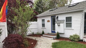 A single-story house with a front porch, a blue door, and a small front yard with a gravel path leading to the door. - Beautiful Free-Standing Cottage, In The Heart of Provincetown.  (Provincetown)