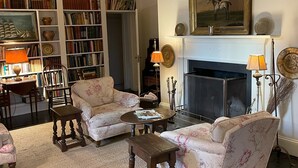 A cozy living room with floral-patterned sofas, a fireplace, bookshelves, and a painting.
