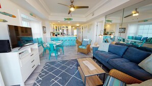 A modern living room with a blue sofa, teal chairs, a wooden coffee table, and a TV.