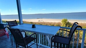 A covered outdoor seating area with a table and chairs, overlooking a beach with people and a motorcycle.