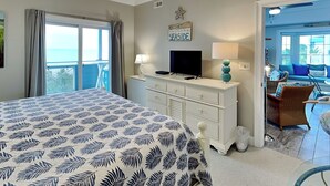 A hotel room with a large bed, a TV, a desk, and a balcony with a view of the sea.
