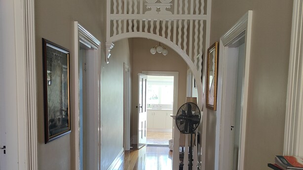 A hallway with wooden floors, white walls, and a decorative white railing. There is a fan and a framed picture on the wall. - Hawthorn House Launceston (Invermay)