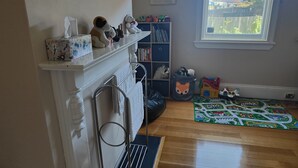 A room with a fireplace, a bookshelf, a window, and a play mat. - Hawthorn House Launceston (Invermay)