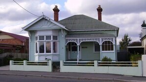 A light blue house with a gabled roof, two chimneys, and a front porch with a white railing. - Hawthorn House Launceston (Invermay)