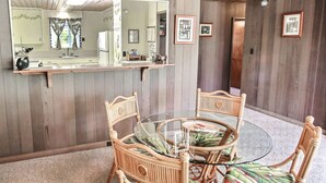 A dining area with a glass-top table and wicker chairs, wooden walls, and framed pictures on the wall.