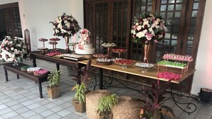 Un tavolo apparecchiato con diversi dolci e composizioni floreali, circondato da cesti di vimini con piante.