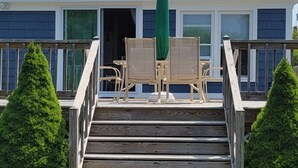 A wooden staircase leading to a house with a green umbrella, a small table, and two chairs on the porch. - Immaculate Cottage, Huge Deck And Great Back Yard For All Your Yard Games. (Middletown)